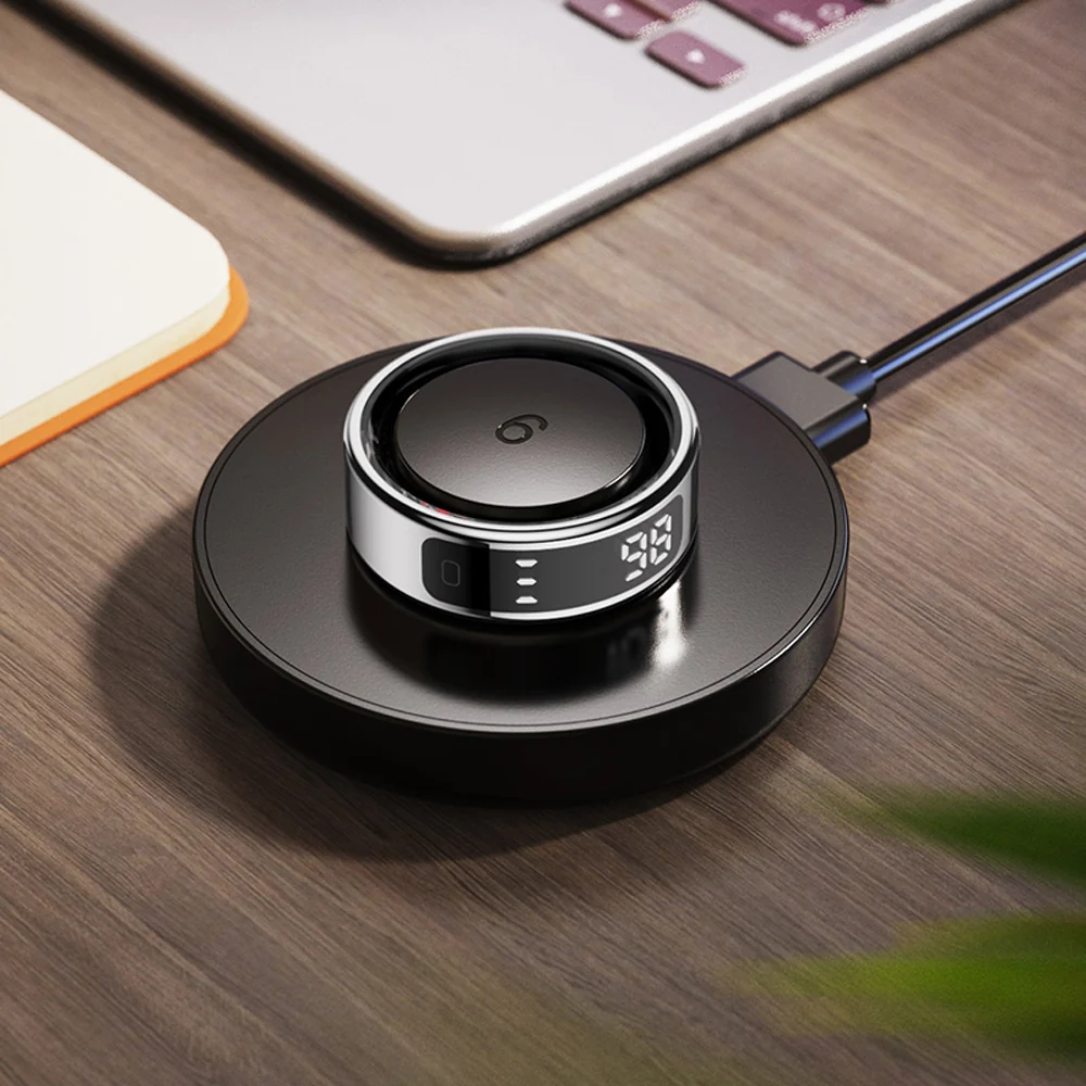 COLMi R12 Smart Ring – Wireless Charging Display COLMi R12 smart ring on a black charging dock with an illuminated numeric display beside a laptop
