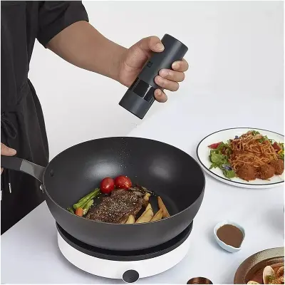 Black Electric Pepper Grinder in Use Person using a black electric pepper grinder to season steak and vegetables in a frying pan