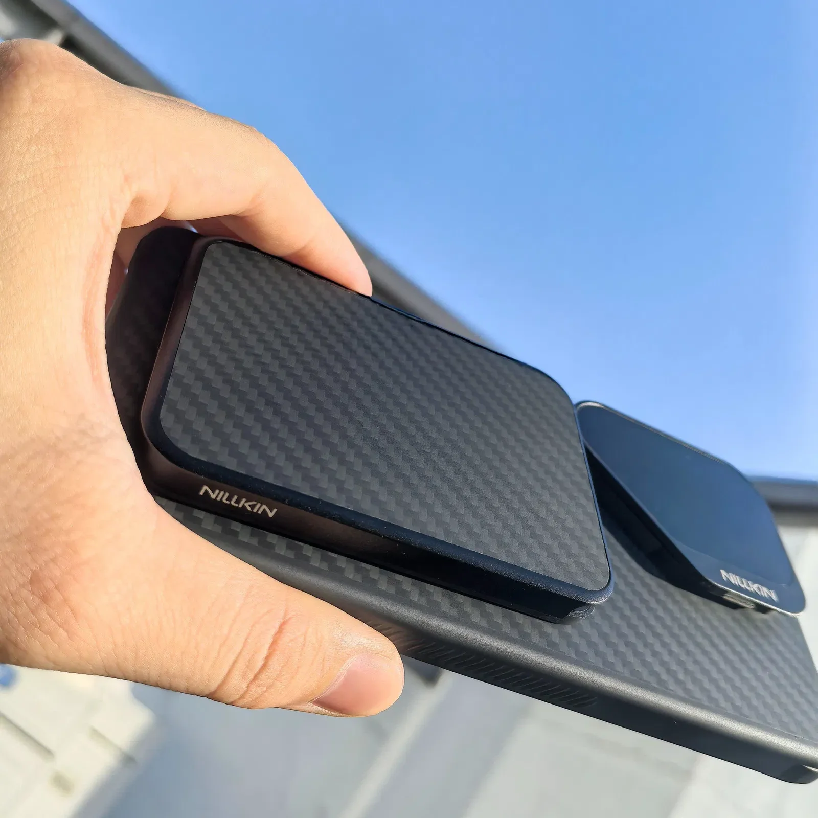 Nillkin FiberMate Wallet Attached to Smartphone Black Nillkin FiberMate wallet attached to a textured smartphone case, held in one hand outdoors.
