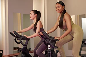 Women Using Indoor Exercise Bikes Two women exercising on stationary bikes in an indoor fitness studio