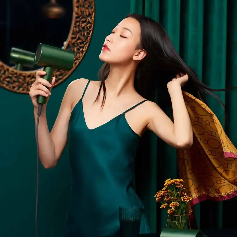 SHOWSEE A5-G Hair Dryer Styling Image Woman holding a green SHOWSEE A5-G hair dryer while lifting her long hair beside a decorative mirror