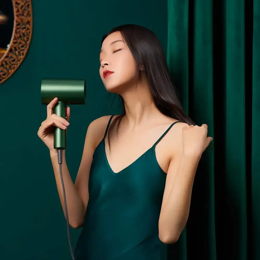 SHOWSEE A5-G Hair Dryer Rear Lifestyle View Woman holding a green SHOWSEE A5-G hair dryer beside her long hair against a dark green background