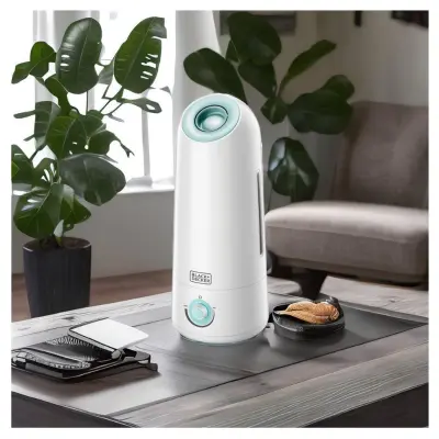 BLACK+DECKER HM5000-B5 Humidifier Living Room Display White BLACK+DECKER HM5000-B5 humidifier on a coffee table beside indoor plants and a grey armchair