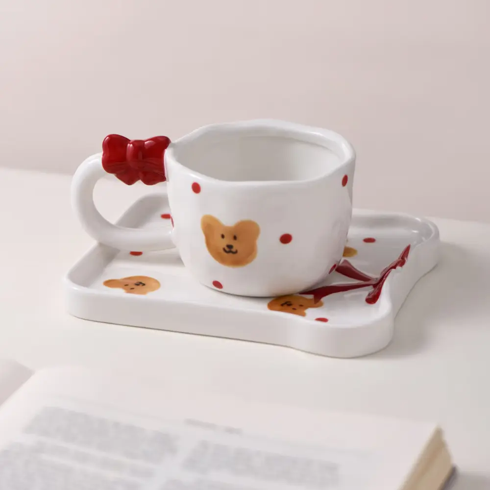Bow and Bear Cup Set Beside a Book White bear-pattern cup with red bow handle on a matching tray beside an open book