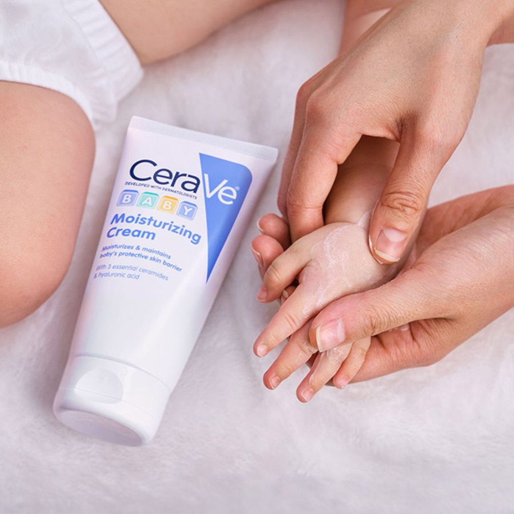 CeraVe Baby Moisturizing Cream Application An adult gently applying cream to a baby’s hand beside a CeraVe Baby Moisturizing Cream tube